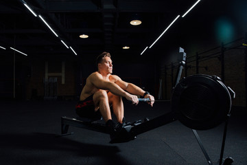 Fitness young man using rowing machine in the gym