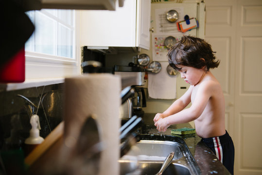 little boy wrings out a sponge at the kitchen sink