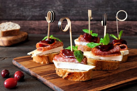 Holiday crostini skewers with cranberry sauce, brie, salami, and mint on a wooden server