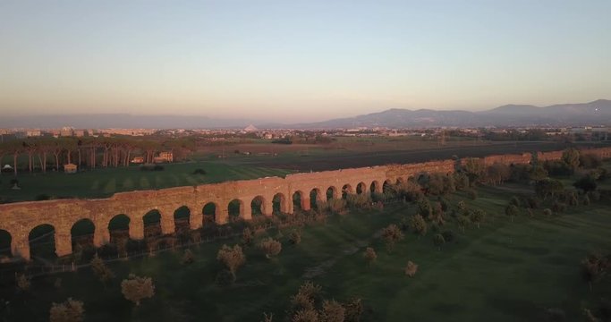 Video from above. Aerial view of the ancient Roman Aqueduct at sunset. Old ruins surrounded by a green public Park. Rome, Italy.