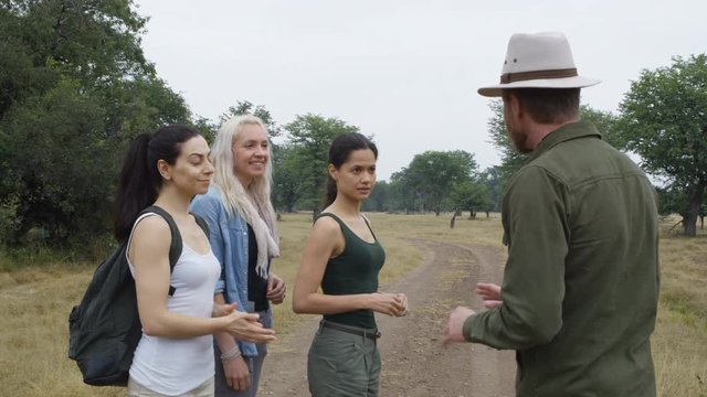  Female friends on safari holiday observing animals & listening to tour guide