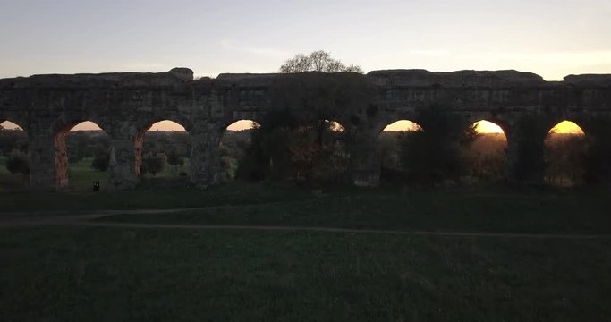 Video from above. Aerial view of the ancient Roman Aqueduct at sunset. Old ruins surrounded by a green public Park. Rome, Italy.