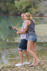 young couple angling standing on river shore