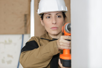 happy female worker using a battery drill in a wall