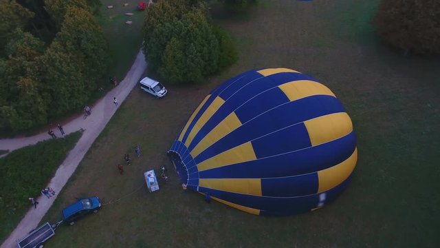 People inflating outspread hot air balloon envelope on ground, preparing flight