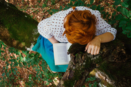 Young ginger girl reading a book while sitting on branch