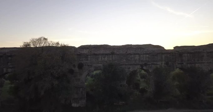 Video from above. Aerial view of the ancient Roman Aqueduct at sunset. Old ruins surrounded by a green public Park. Rome, Italy.