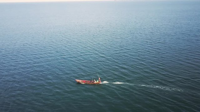 Aerial camera looking down on a small fishing boat motoring through the sea and then lowers to an angle that shows the horizon and more islands in the distance as the camera tracks with the boat.