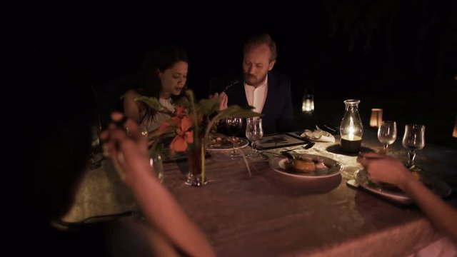  Friends on vacation enjoying a meal at candlelit outdoor restaurant table