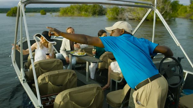  Tourists on boat trip on the Zambezi river listening to tour guide