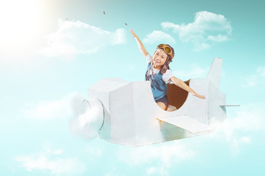 Little cute girl fly with a white retro style cardboard airplane on sky . Childhood dream imagination concept .