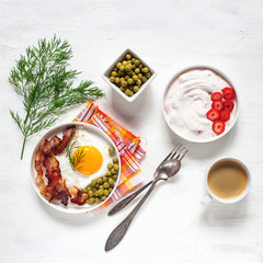 Breakfast - fried eggs with bacon and green peas, coffee and cottage cheese with strawberry on a light background. Selective focus. Top view. Flat lay