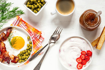 Breakfast - fried eggs with bacon and green peas, coffee and cottage cheese with strawberry on a light background. Selective focus. Top view. Flat lay