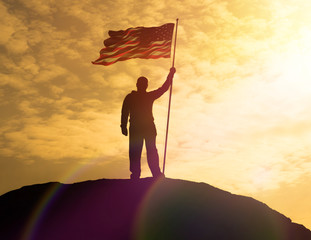 Silhouette of man holding US flag American on the mountain. The concept of Independence Day. a...