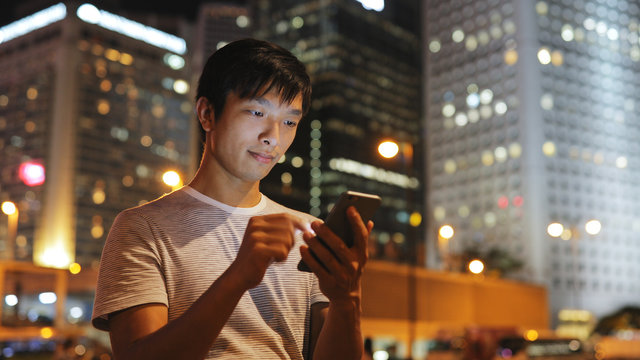Young Man Using Mobile Phone In City At Night