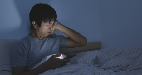 Asian man using cellphone and feeling eye dried