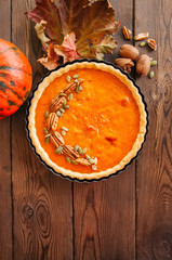 Pumpkin pie - traditional american dessert garnished with pecans and seeds on a wooden background
