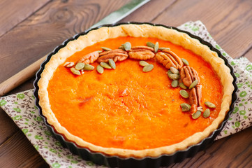 Pumpkin pie - traditional american dessert garnished with pecans and seeds on a wooden background