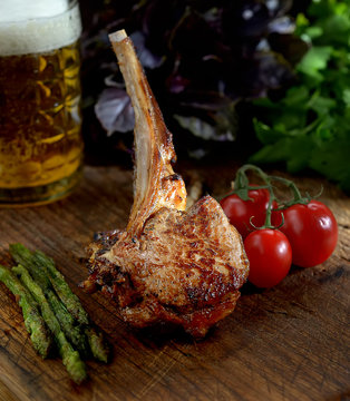 grilled lamb steak with asparagus and tomatoes on a wooden background