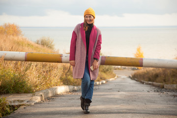 Young beautiful brunette woman in yellow knitted headband, pink coat and jeans smiling and posing...