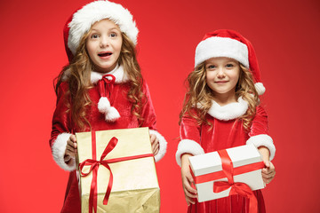 Two happy girls in santa claus hats with gift boxes at studio