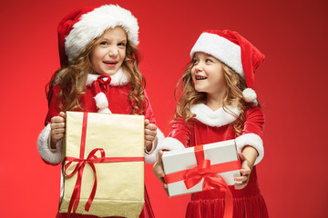 Two happy girls in santa claus hats with gift boxes at studio