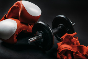 Red boxing gloves, barbell and boxing wraps with dark background.