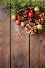 Christmas background. Fir tree branches, red and golden balls and cones on a wooden backdrop.
