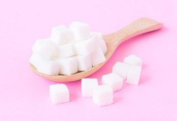Closeup sugar cubes on wooden spoon with pink background, health care concept
