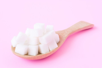 Closeup sugar cubes on wooden spoon with pink background, health care concept