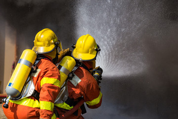 Fototapeta premium two firefighters water spray by high pressure nozzle surround with dark smoke and copy space