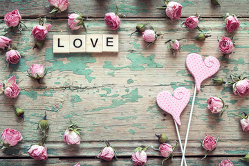 Background of small pink roses, hearts and word love on old wooden boards. Space for text.