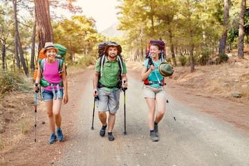 Multinational group of young happy friends students traveling along the Lycian trail with backpacks at the coastal road in the forest. Hiking and trekking in Turkey concept