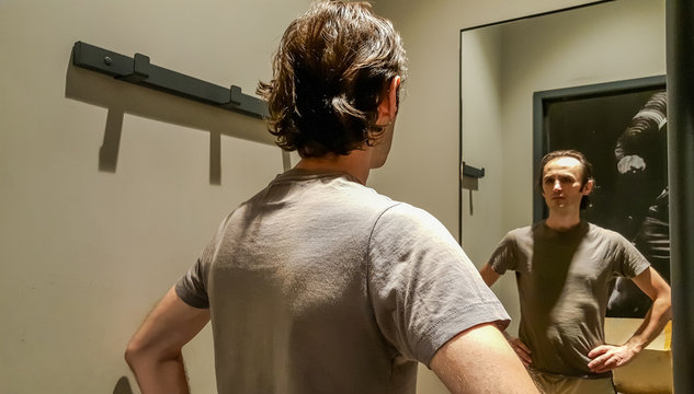 Rear view of a young Caucasian handsome man trying new clothes in front of a mirror in a changing room of a clothing store