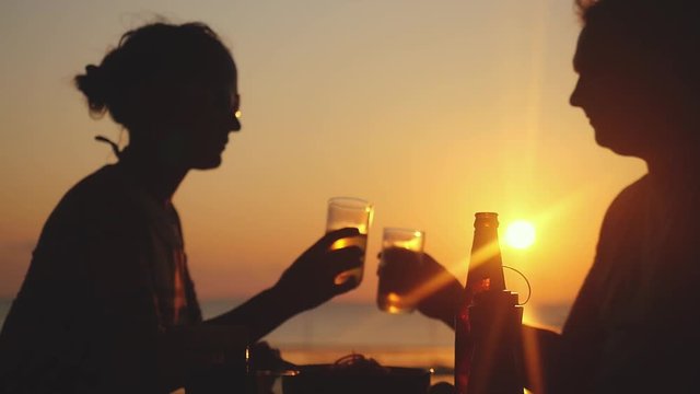 Young happy couple clinking glasses drink beer in beach cafe at amazing sunset in slow motion. 1920x1080