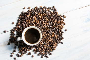 a cup of coffee with coffee seed on white wood background