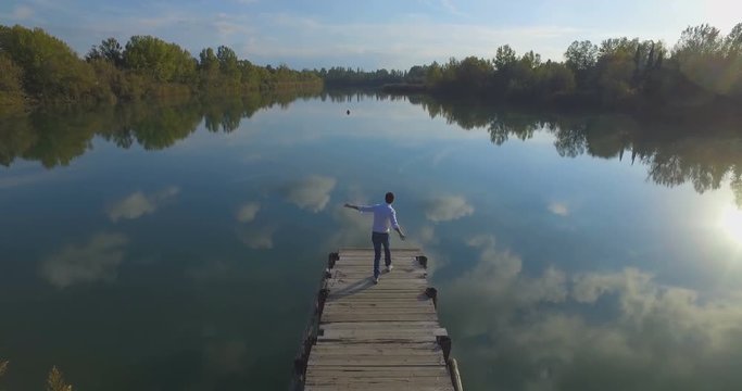 Giovane ragazzo sta ballando allegramente su un molo di legno di un lago