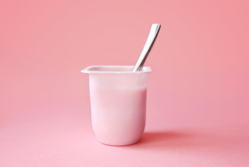 Delicious strawberry yogurt or pudding  in white plastic cup on pink background with copy space. Strawberry pink yoghurt with spoon in it. Minimal style.