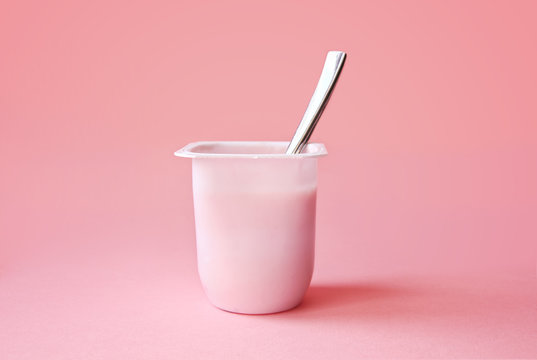 Naklejki Delicious strawberry yogurt or pudding  in white plastic cup on pink background with copy space. Strawberry pink yoghurt with spoon in it. Minimal style.