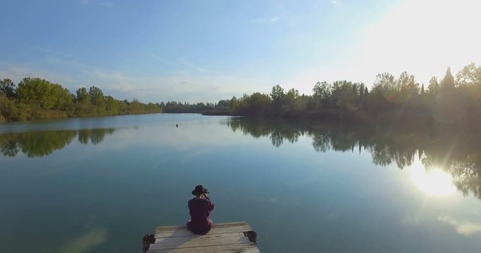 Giovane ragazzo con barba e cappello sta camminando su un molo di legno in riva a un lago 