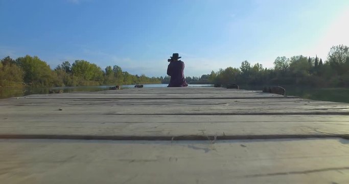 Giovane ragazzo con barba e cappello sta camminando su un molo di legno in riva a un lago 