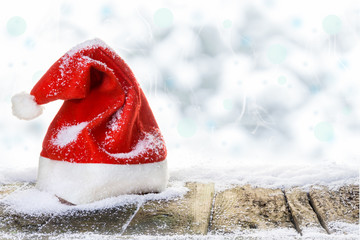 Weihnachtsmütze auf verschneitem Holzboden vor Winterhimmel mit Bokeh