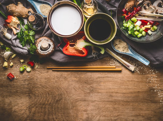 Vegetarian stir fry ingredients with coconut milk, soy sauce and chopsticks on wooden background, top view, border. Asian food , Chinese or Thai cuisine concept
