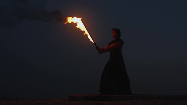Silhouette of hispanic man with fire sword at night, martial arts, waving a sword slow motion