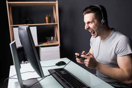 angry screaming young man in headset with pc computer playing game at home and streaming playthrough or walkthrough video