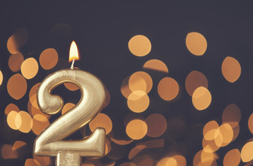 Gold number 2 celebration candle against blurred light background