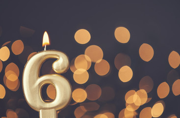 Gold number 6 celebration candle against blurred light background