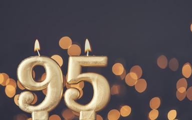 Gold number 95 celebration candle against blurred light background