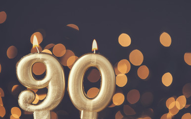 Gold number 90 celebration candle against blurred light background