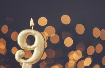 Gold number 9 celebration candle against blurred light background